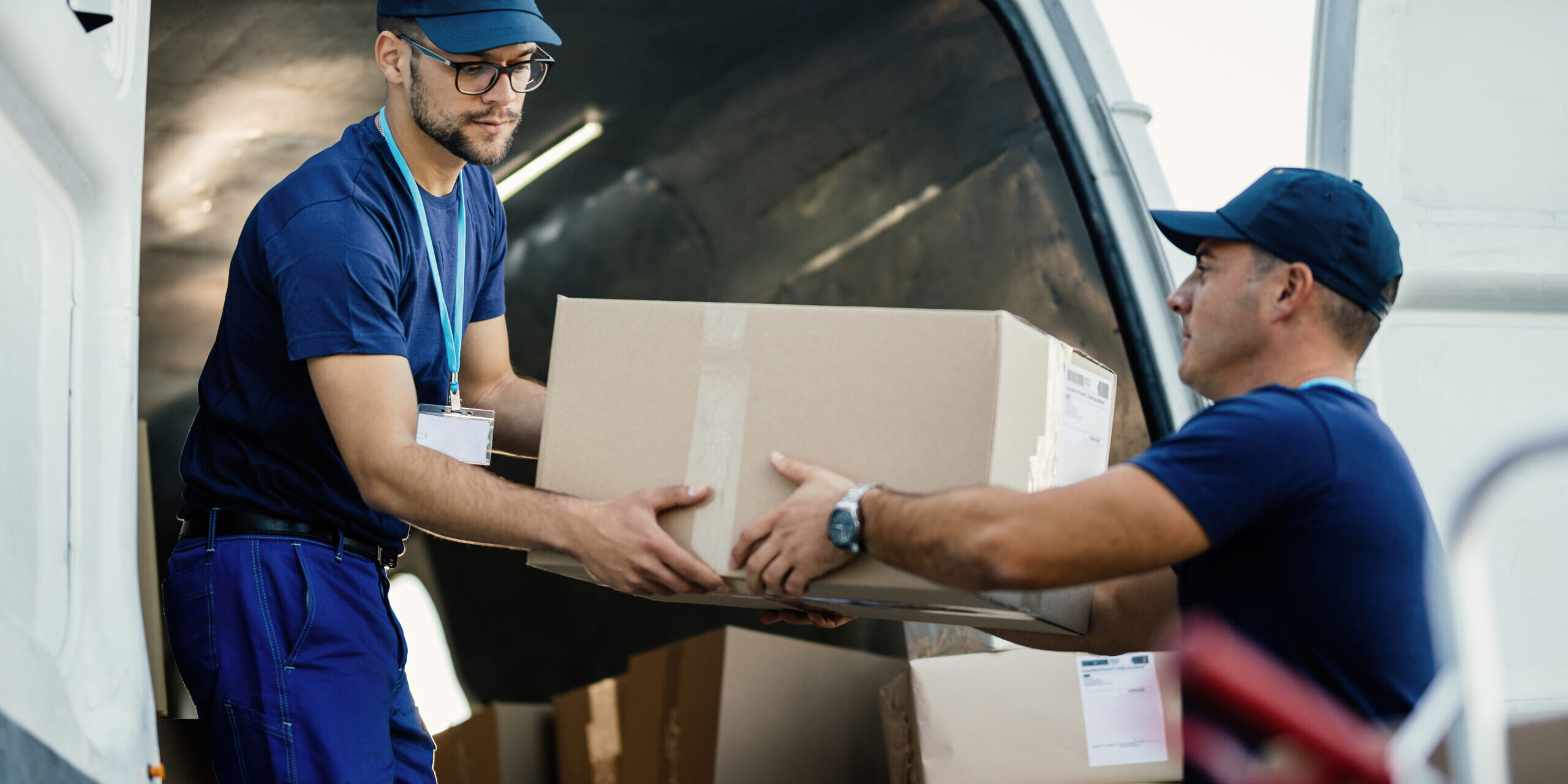 Young couriers cooperating while unloading packages from deliver